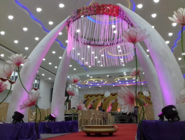 An elegant wedding stage adorned with floral arrangements, a grand chandelier, & soft purple lighting