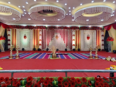 A decorated event stage with red and white drapes, floral arrangements, and elegant lighting.