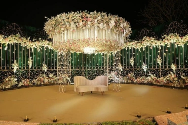 A flower chandelier hangs above a bench, framed by intricate decorative gates, glowing at night.