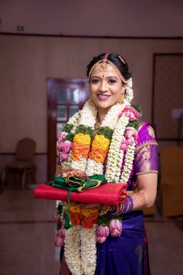 A bride in traditional Indian attire, holding a vibrant red and purple bouquet at her wedding.