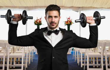 Man in formal attire holding dumbbells symbolizing the balance of health and well-being at a wedding