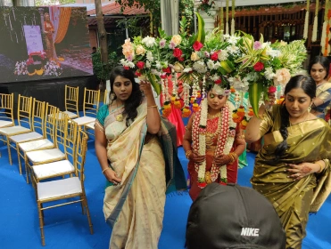 Many people were in traditional attire at an event with floral decorations and arranged chairs.