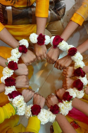 Eight hands join to form a circle, adorned with white & red floral wristbands, creating a display.