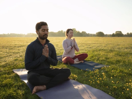 Two people meditating in a serene field, finding calm amid wedding excitement and stress