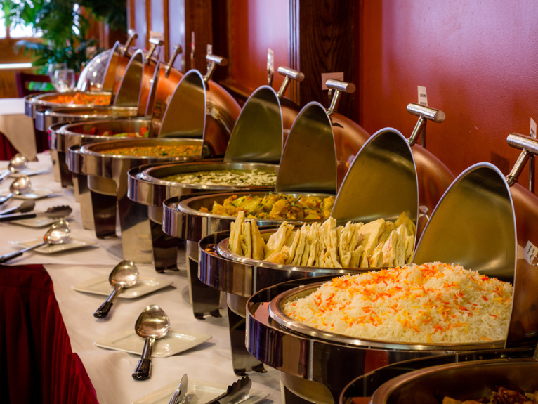 A row of copper food domes with intricate patterns is displayed on a buffet, reflecting light beautifully.