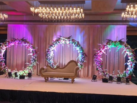 An ornate stage was arranged with a grand floral arch and suitable chairs for a wedding setting.