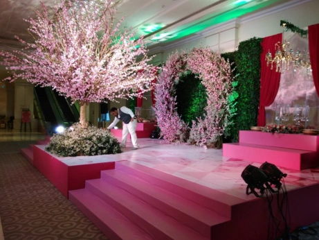 Modern decorations enhance the vibrant atmosphere of a stage adorned with pink flowers and a tree.
