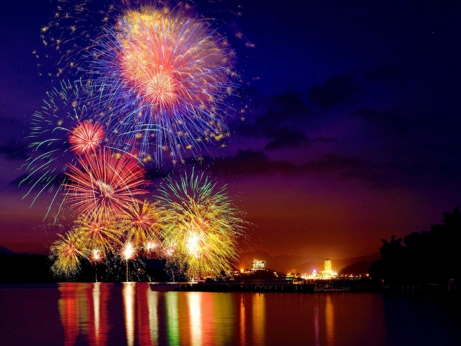 Fireworks burst over the water with a dazzling display of colorful hues, creating a stunning scene.