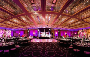 In a grand ballroom, twinkling lights cover the ceiling in purple, creating a romantic atmosphere.