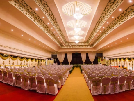 A large hall with tables and chairs arranged for a occasion, curated by Mandapam Wedding Planners.